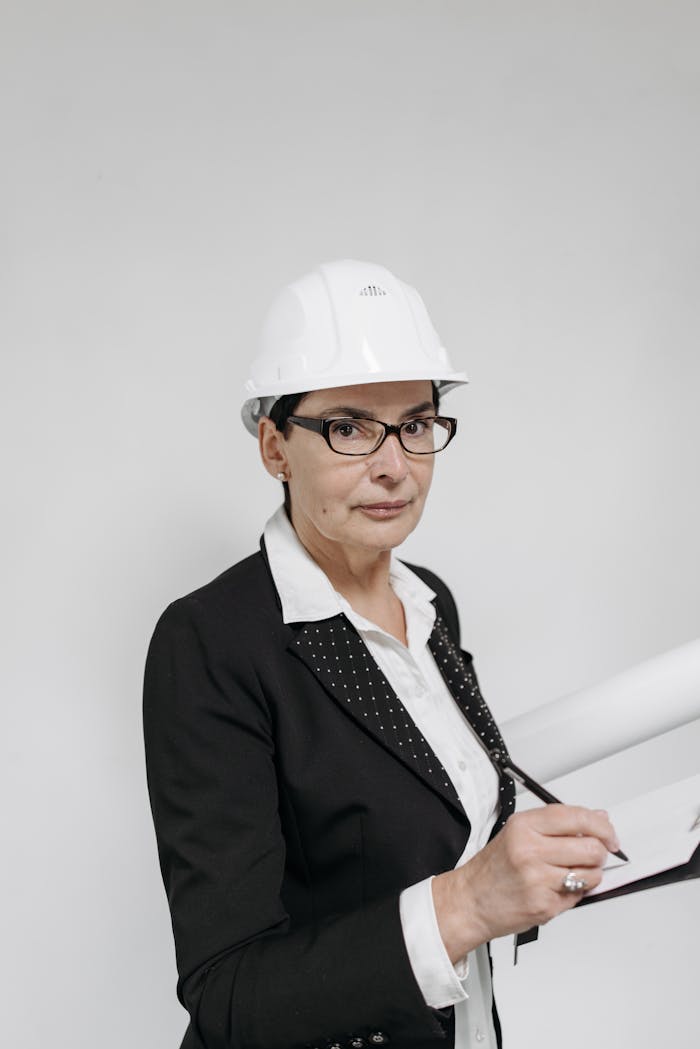 Confident woman architect in a formal suit holding building plans indoors.